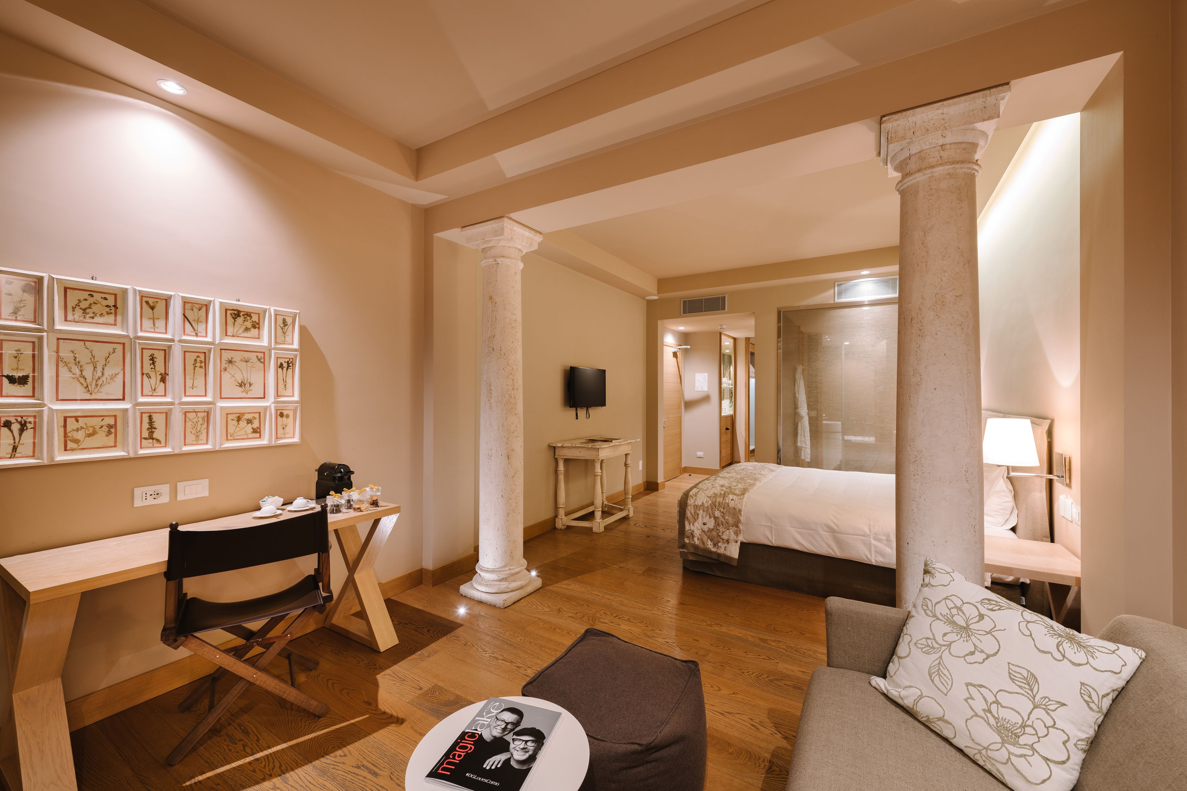 Habitación de hotel con escritorio, cama, sofá e imágenes botánicas enmarcadas en la pared.