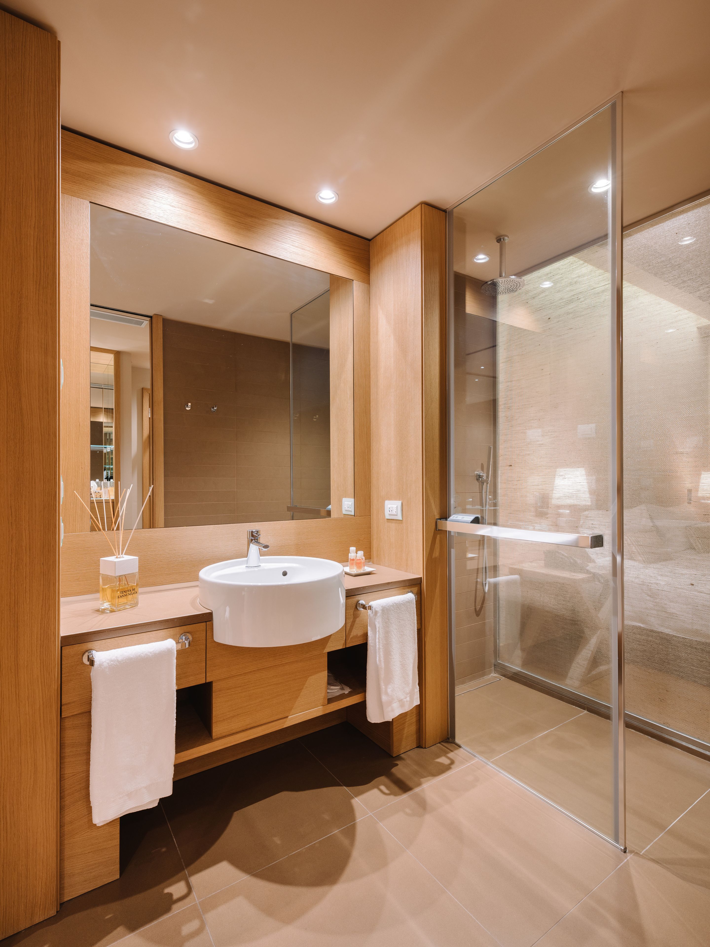A modern bathroom with a large mirror, wooden vanity, white sink, and a glass shower enclosure.