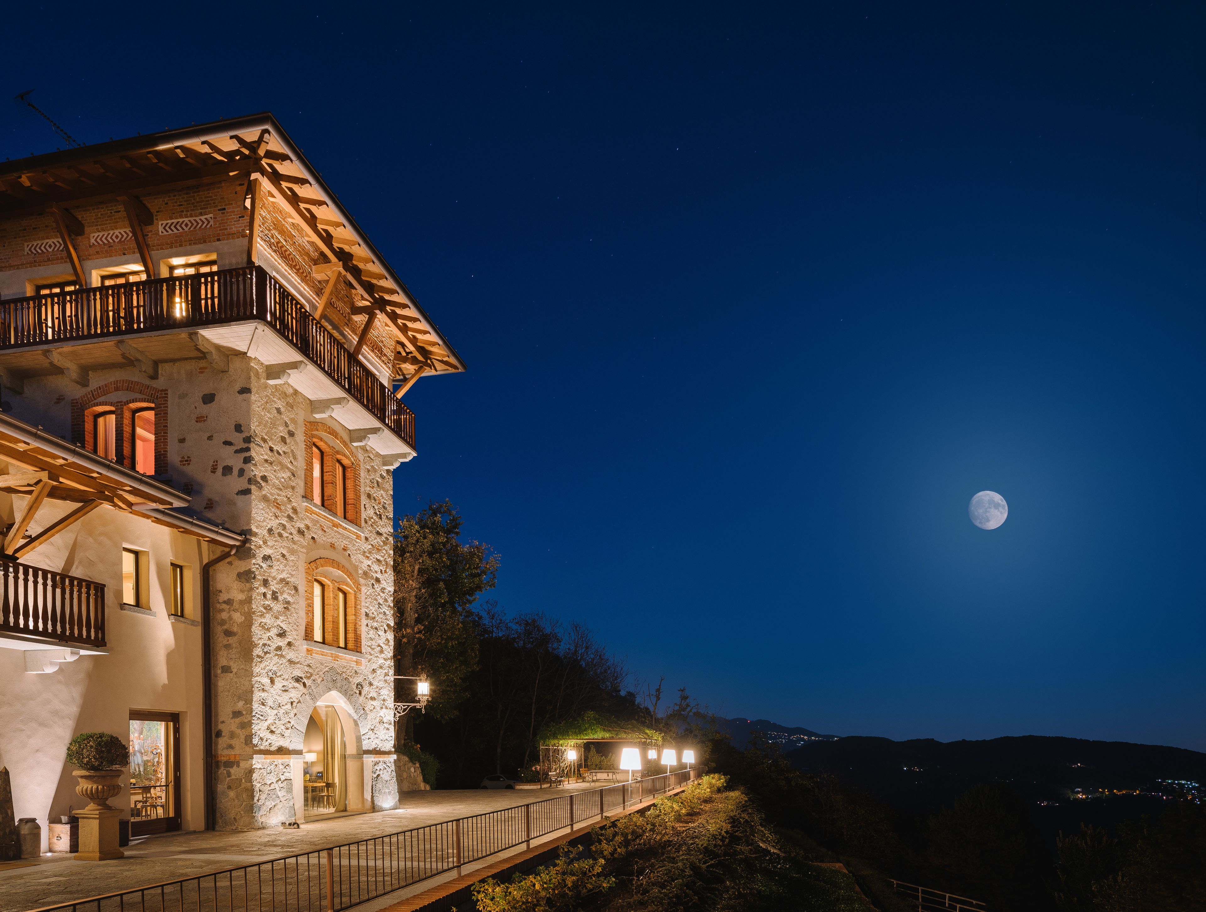 Un edificio de piedra con un balcón, la luna en el cielo y vistas del paisaje.