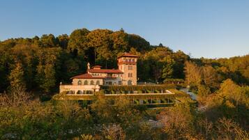 A large, historic building with a tower, surrounded by dense forest and a well-maintained garden.
