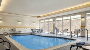 An indoor swimming pool with tiled walls, a brick wall in the background, and a seating area with chairs and tables. - Fairfield Inn & Suites Bristol (Bristol)
