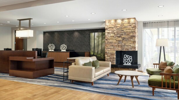 A modern hotel lobby with a reception desk, seating area, stone fireplace, and large windows. - Fairfield Inn & Suites Bristol (Bristol)