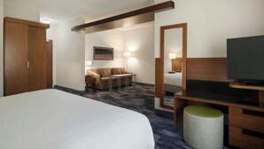A hotel room with a large bed, a desk with a television, a sofa, and a mirror. - Fairfield Inn & Suites Bristol (Bristol)