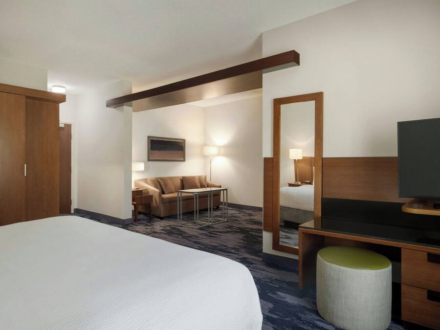 Ein Hotelzimmer mit einem großen Bett, einem Schreibtisch mit Fernseher, einer Sitzecke und einem Spiegel.