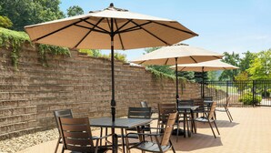 An outdoor patio with brick flooring, metal tables and chairs, and beige umbrellas providing shade. - Fairfield Inn & Suites Bristol (Bristol)