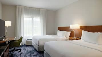 A hotel room with two beds, a desk with a chair, a TV, and a window with curtains.