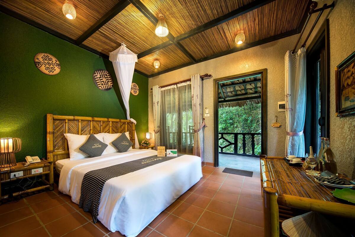 Een ruime slaapkamer met een groot bed, een houten hoofdbord en een balkon met uitzicht op groen.