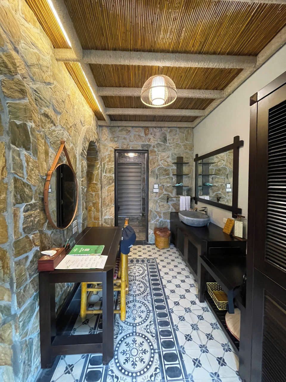 A bathroom with stone walls, a wooden ceiling, a sink, a mirror, and a patterned floor.