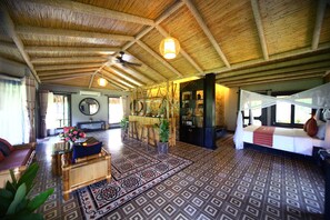 A spacious living area with a high ceiling, a central seating area with a sofa and chairs, a dining table with stools, and a patterned floor.