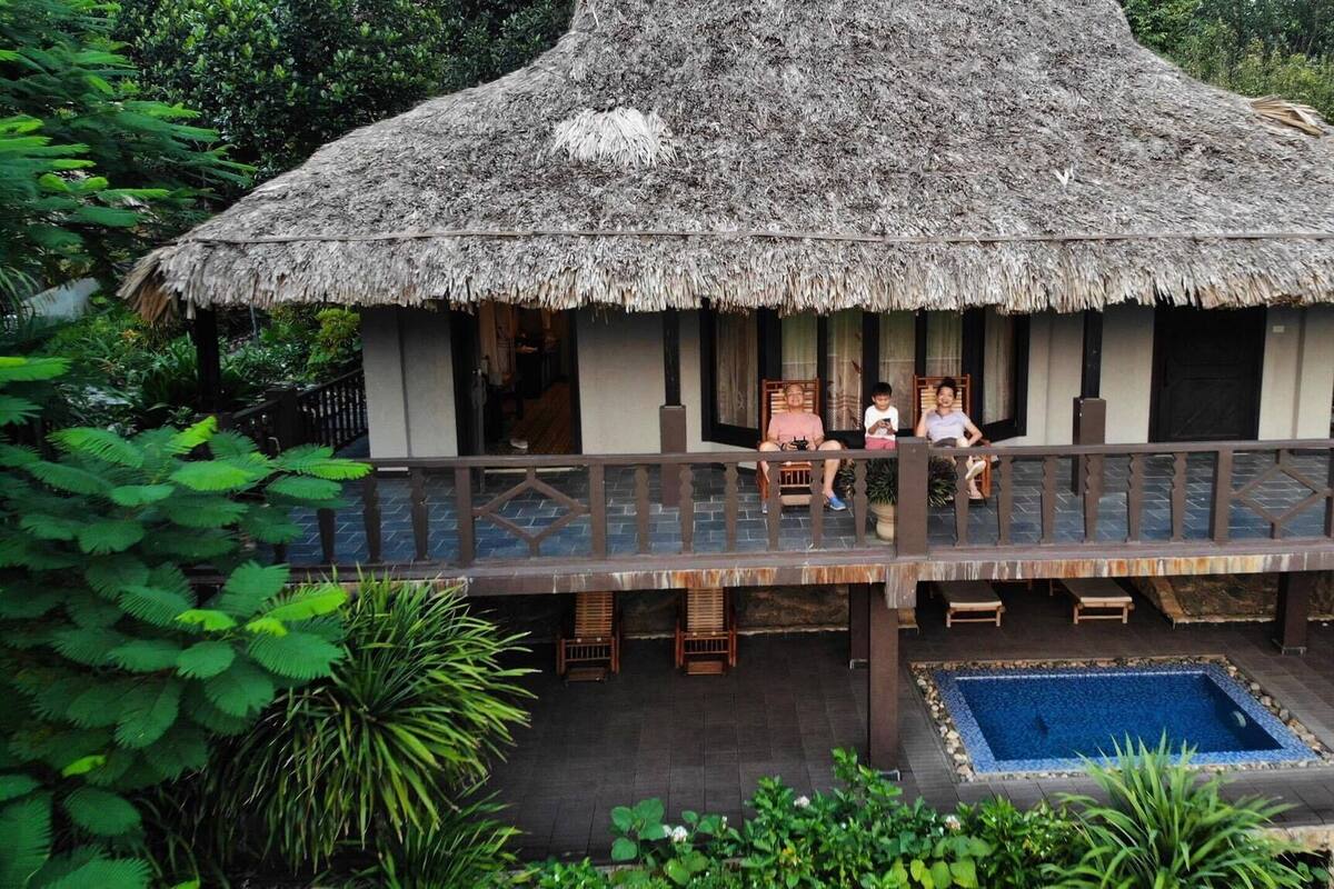 Een rieten huis met een balkon dat uitkijkt over een zwembad.