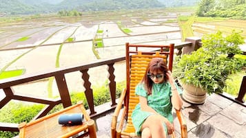 A person seated on a wooden chair with a view of terraced fields and mountains in the background.