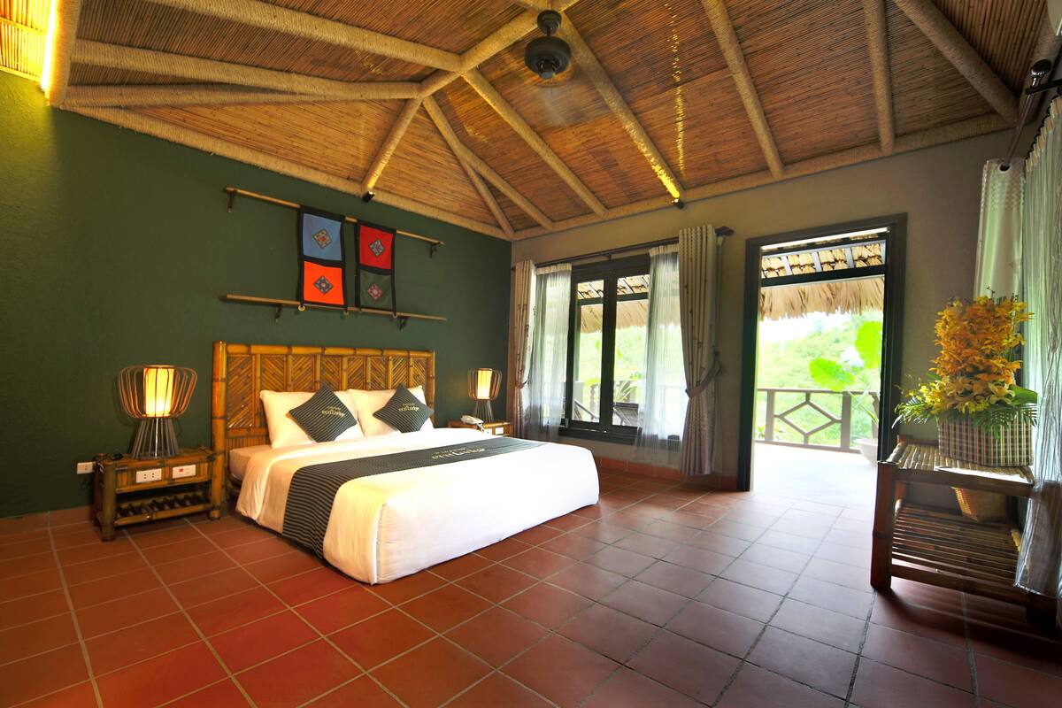 Een ruime slaapkamer met een groot bed, een houten plafond en uitzicht op de omgeving.