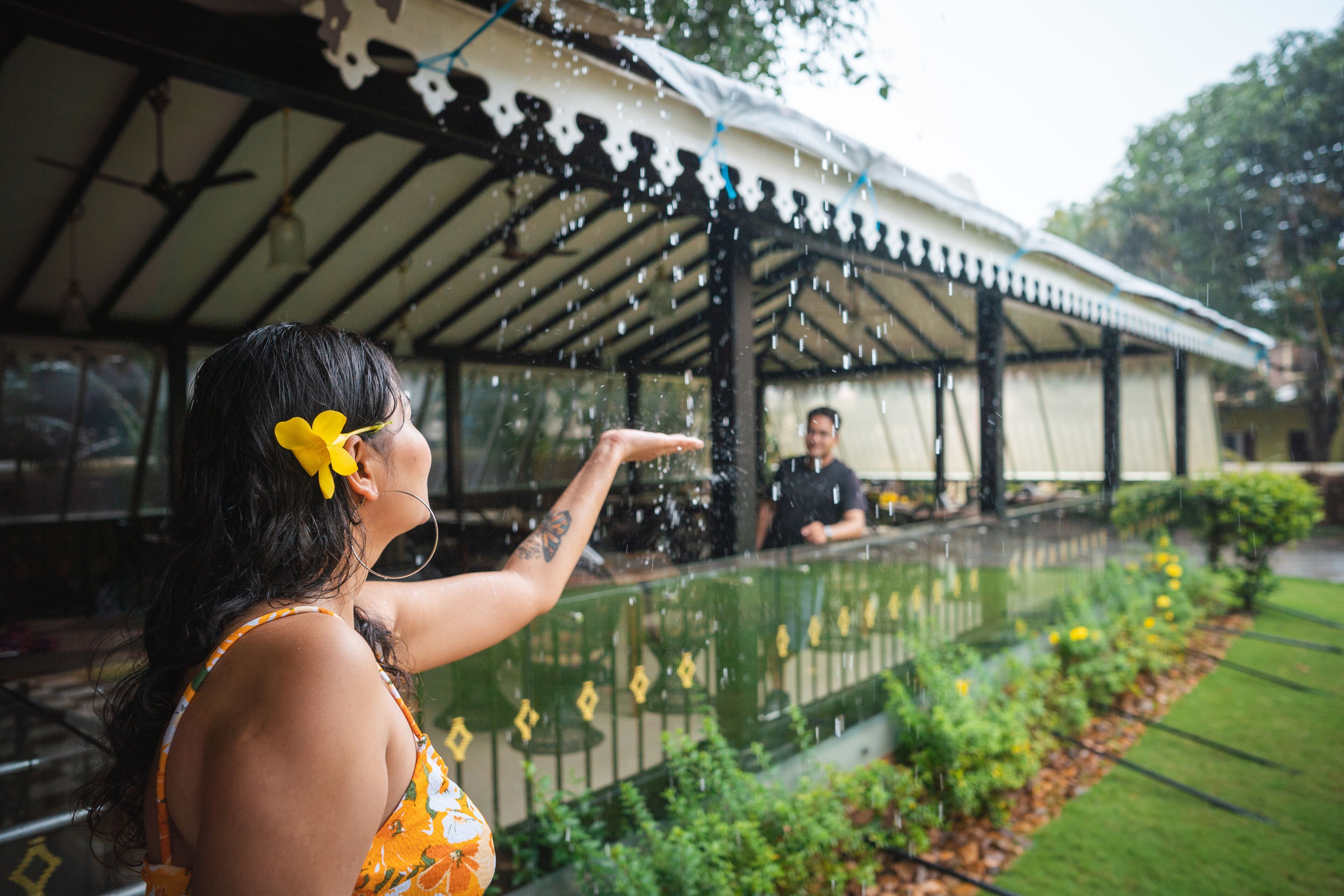 A covered outdoor area with a glass barrier, a person in the foreground, and a person in the background.