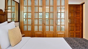Une chambre avec une grande armoire en bois, un lit avec une literie blanche et un miroir au-dessus de l’armoire.