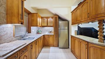 A kitchen with wooden cabinets, a marble countertop, and a stainless steel refrigerator.
