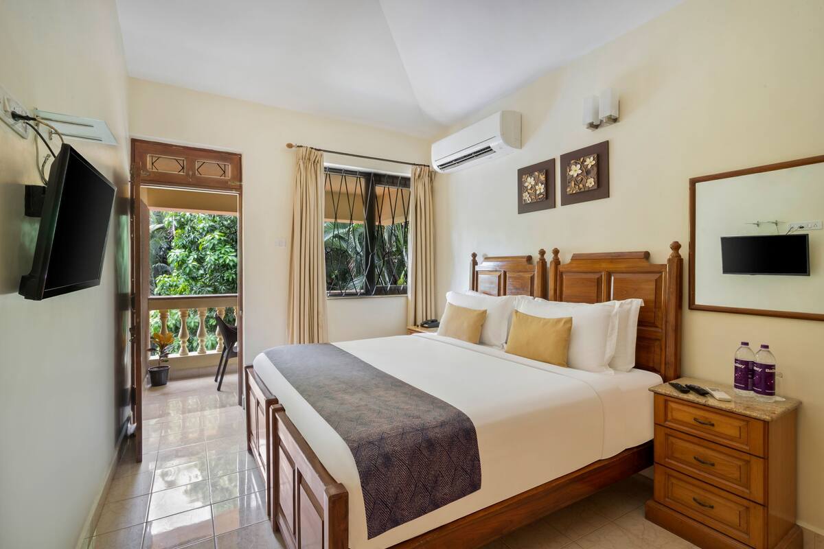 A hotel room with a large bed, a TV, a bedside table, and a window with curtains.