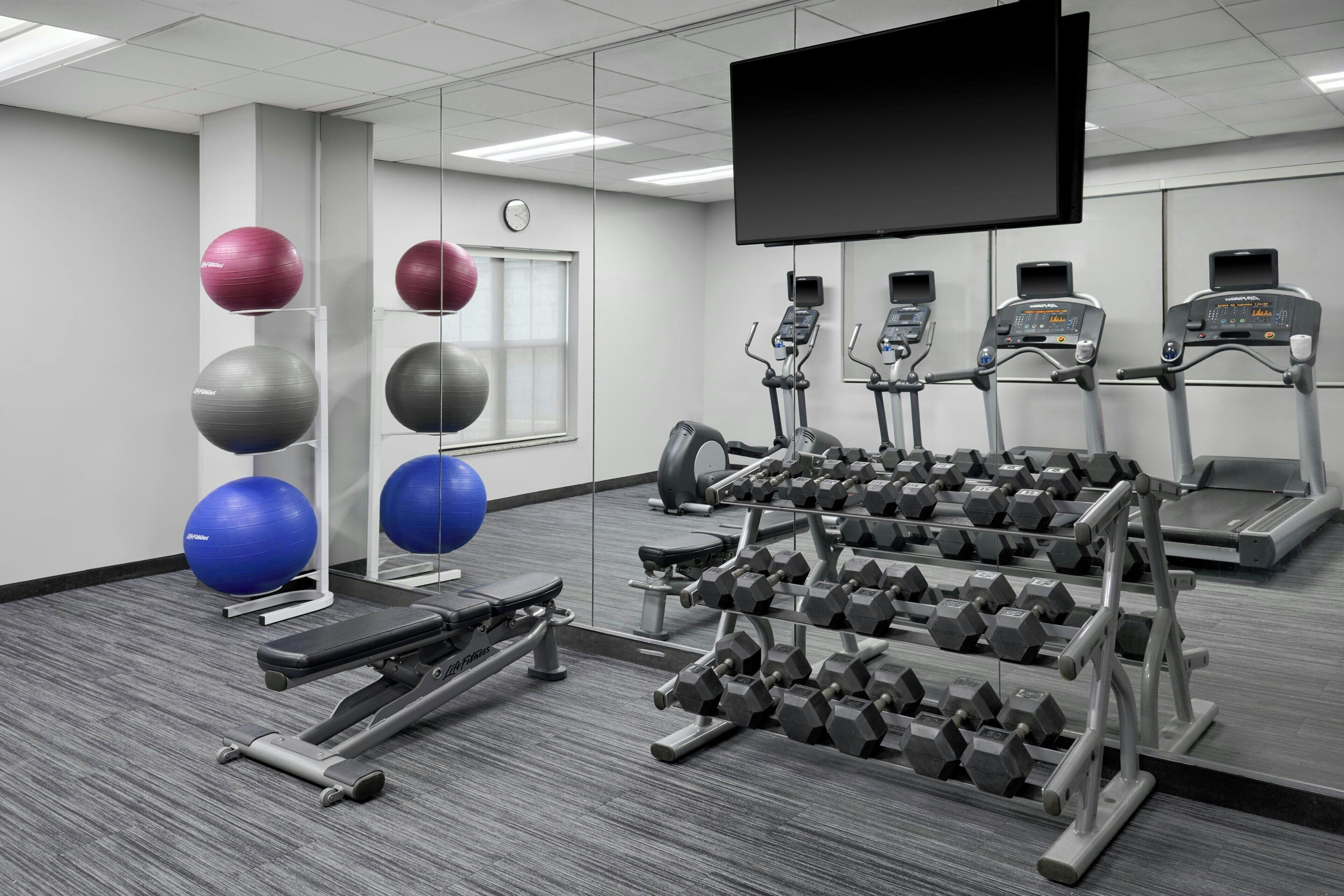 Un gimnasio con cintas de correr, mancuernas y pelotas de ejercicio.