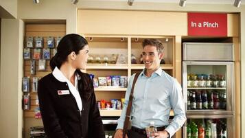A retail store with shelves stocked with products and a refrigerated section in the background.