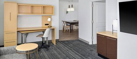 Une chambre d’hôtel moderne équipée d’un canapé, d’une petite table ronde, d’un bureau avec une chaise, d’un coin repas avec une table et des chaises, et d’un téléviseur fixé au mur.