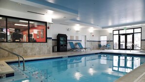 Piscina interior com água cristalina, cadeira de salva-vidas e escada para piscina.