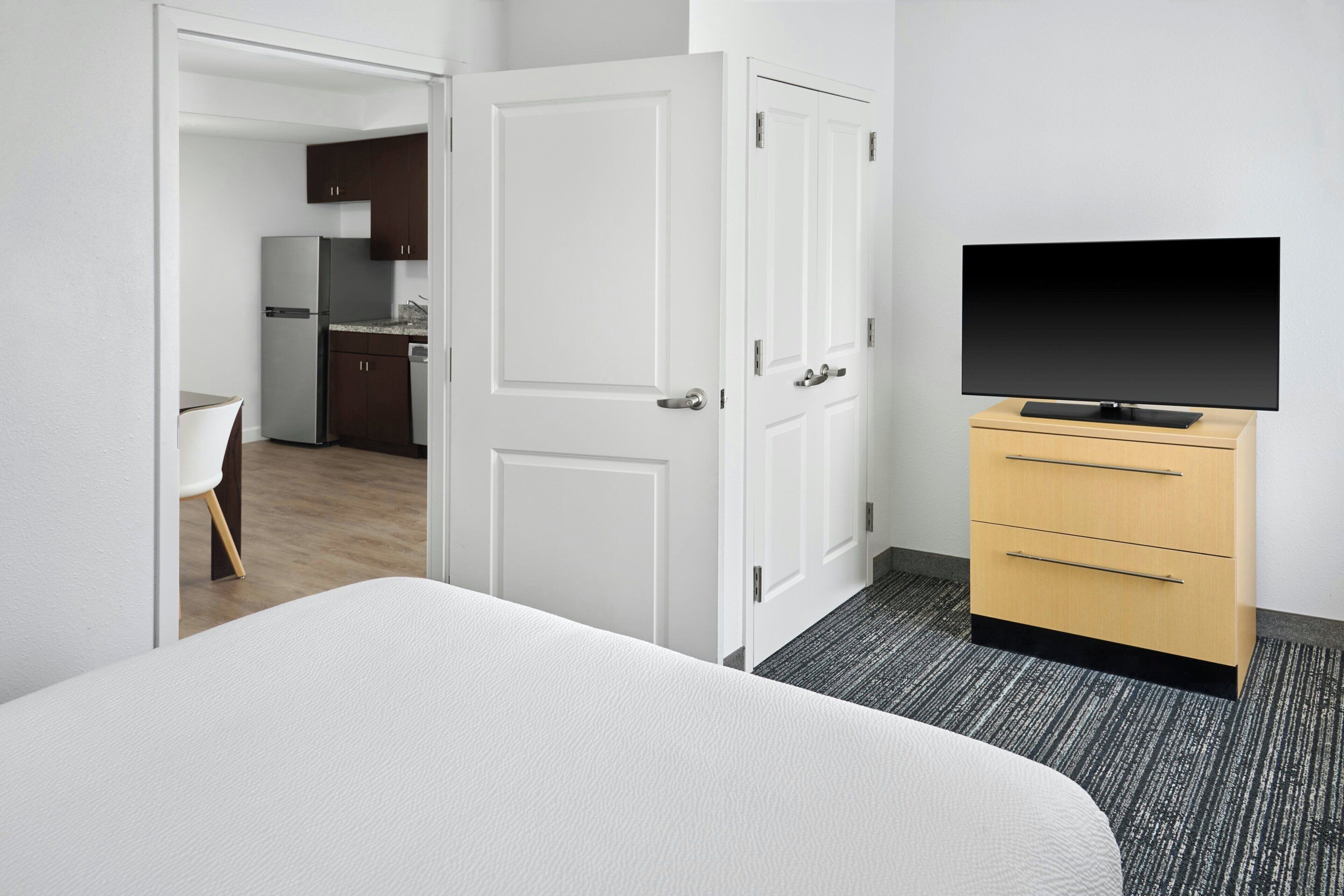 A hotel room with a bed, a TV on a stand, a wardrobe, and a door leading to a kitchen area.