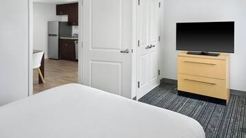 A hotel room with a bed, a TV on a stand, a wardrobe, and a door leading to a kitchen area.