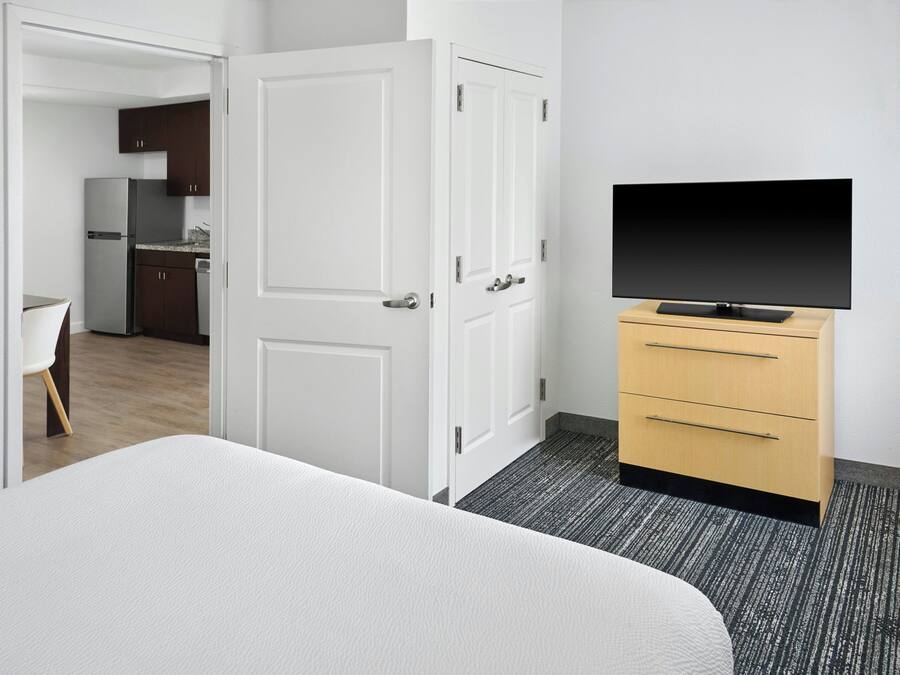 A hotel room with a bed, a TV on a stand, a wardrobe, and a door leading to a kitchen area.