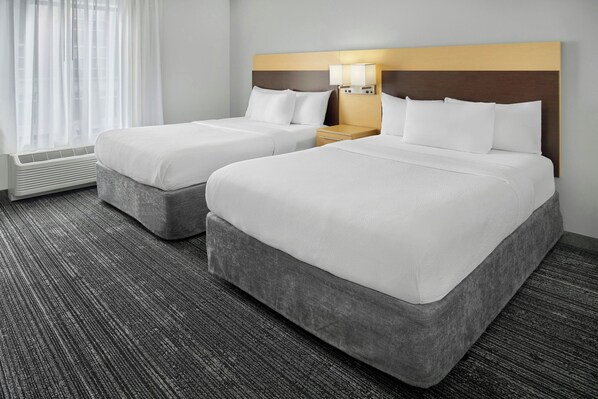 A hotel room with two beds, a bedside table with a lamp, and a window with curtains. - TownePlace Suites Lawrence Downtown (Lawrence)