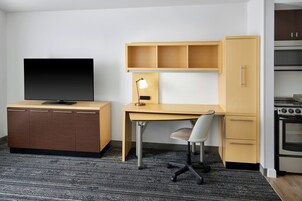 Una habitación compacta con escritorio de madera, una silla, televisor, armario y kitchenette.