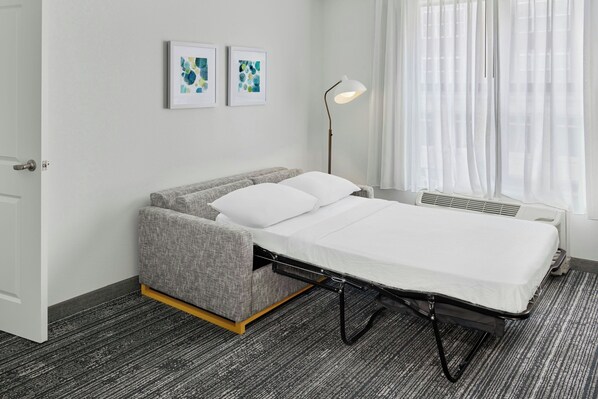 A compact room with a bed, a grey sofa, a floor lamp, and two abstract paintings on the wall. - TownePlace Suites Lawrence Downtown (Lawrence)