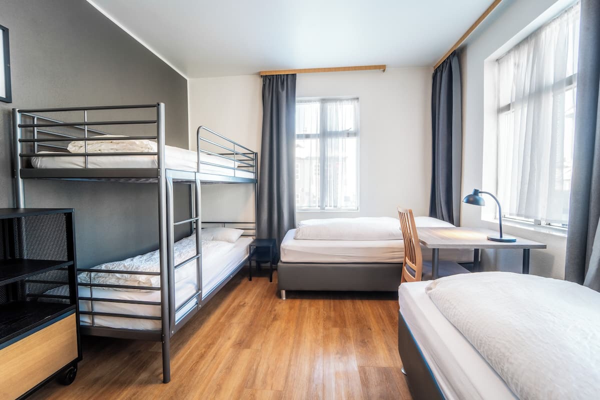A bunk bed room with a desk, chair, and a window with curtains.