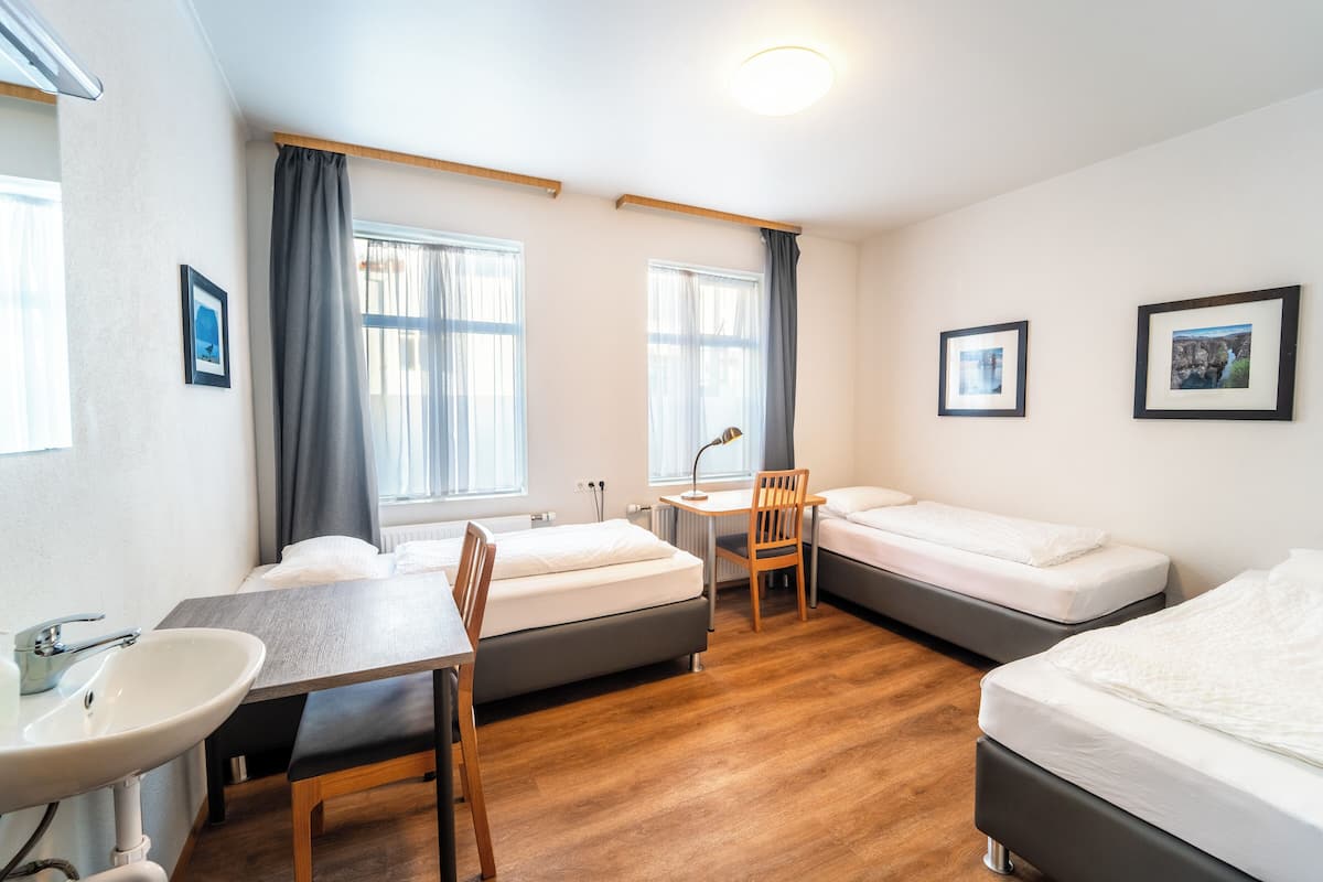 A hotel room with two beds, a desk, a chair, a sink, and two framed pictures on the wall.