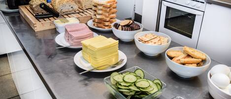 Une table de buffet proposant divers aliments, notamment du pain, du fromage, du jambon et des légumes.