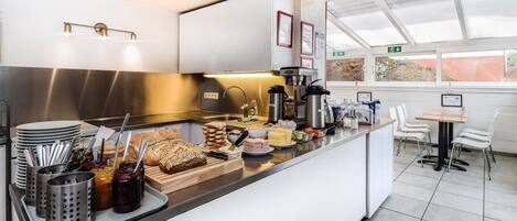 A modern kitchen with stainless steel appliances, a buffet counter with various food items, and a seating area with white chairs and a table.