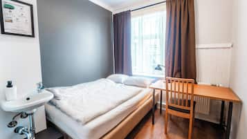 A bedroom with a bed, a wooden table, a chair, a white sink, and a window with curtains.