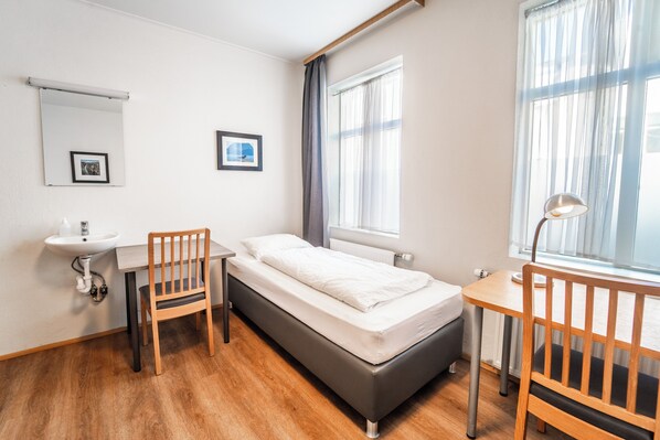 A small, clean room with a bed, a desk, a chair, a sink, and a window with curtains. - Guesthouse Aurora (Reykjavik)