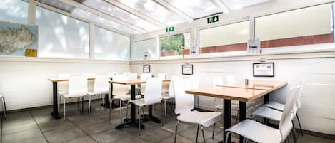 Un salón de conferencias con mesas y sillas, amplias ventanas y carteles informativos en las paredes.