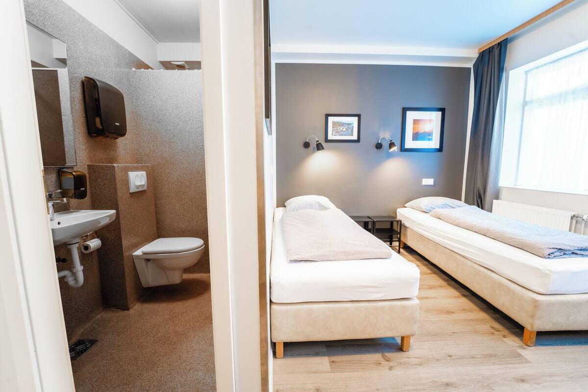 A room with a bed, a bedside table, a mirror, a sink, and a toilet.