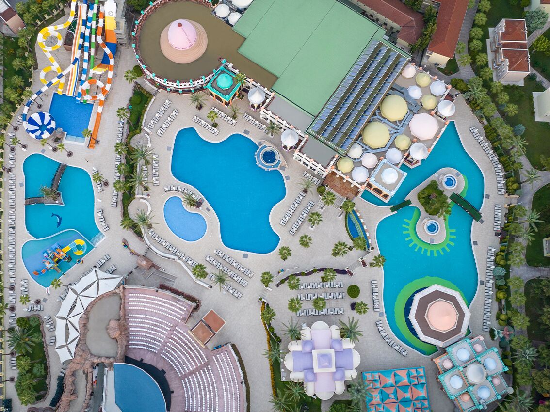 An aerial view of a resort with multiple swimming pools, a water slide, and various recreational areas.