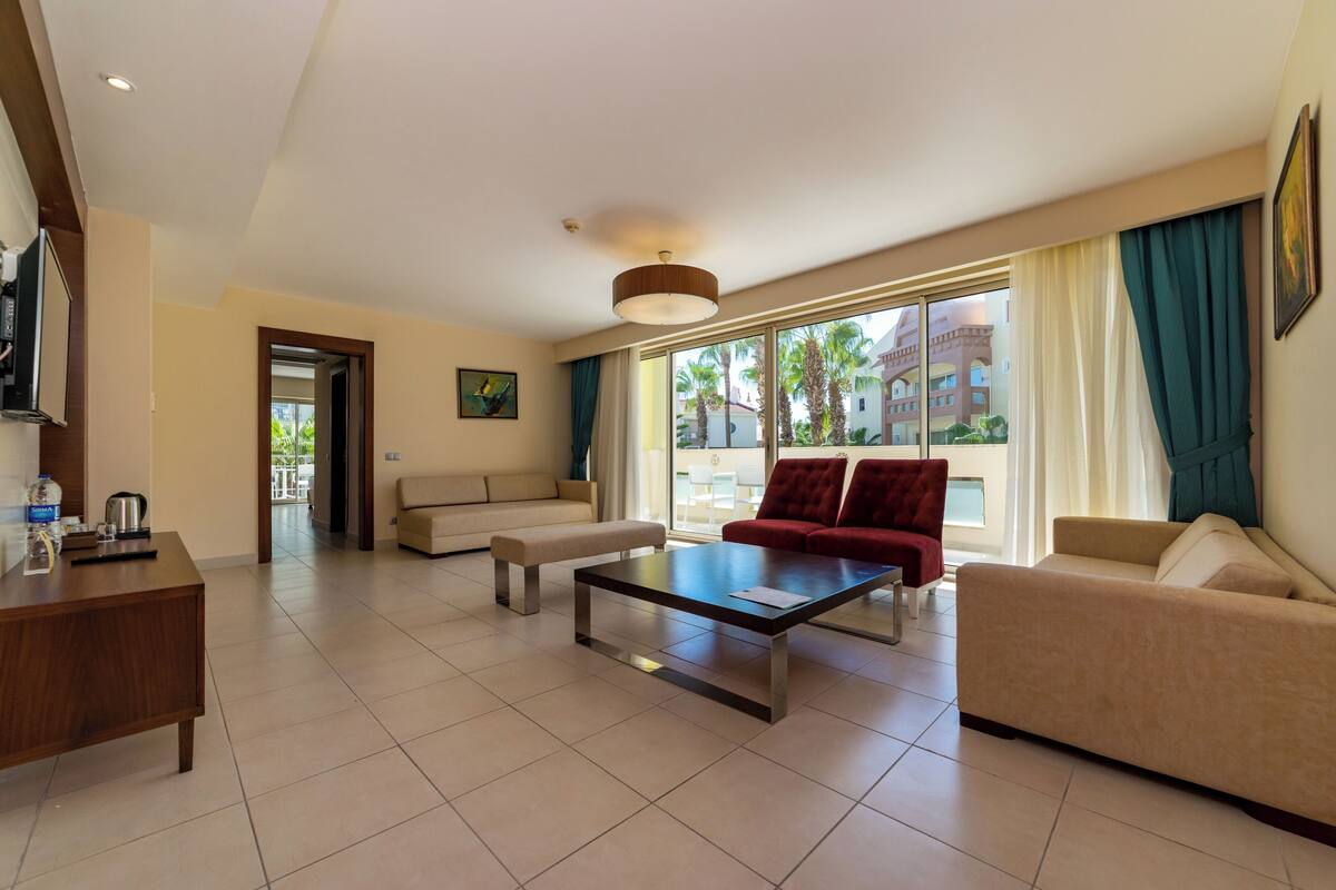 Un salón espacioso con un sofá, un sillón rojo, una mesa de centro y un televisor sobre un mueble de madera.