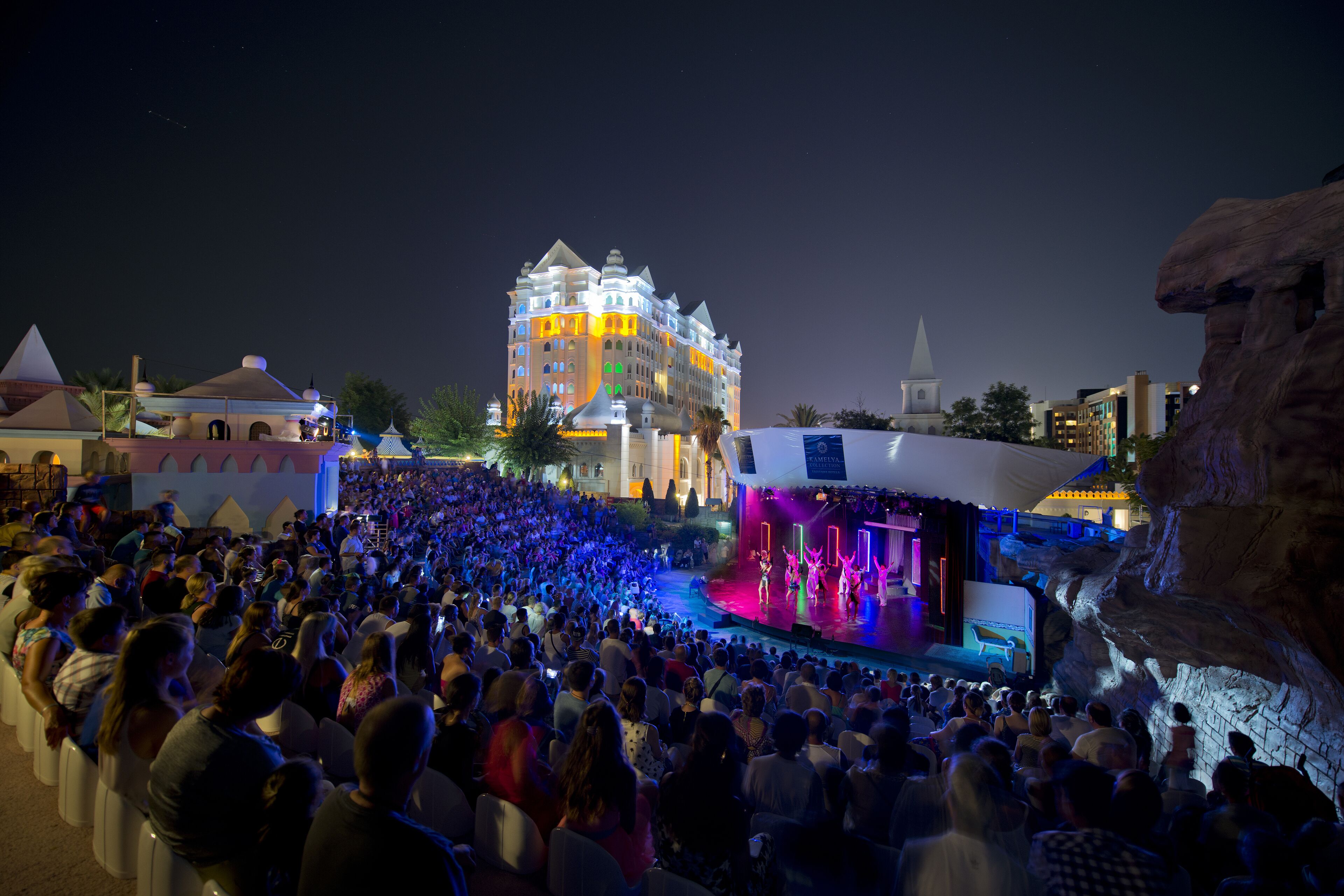 A large outdoor gathering at a venue with a stage and a building in the background.