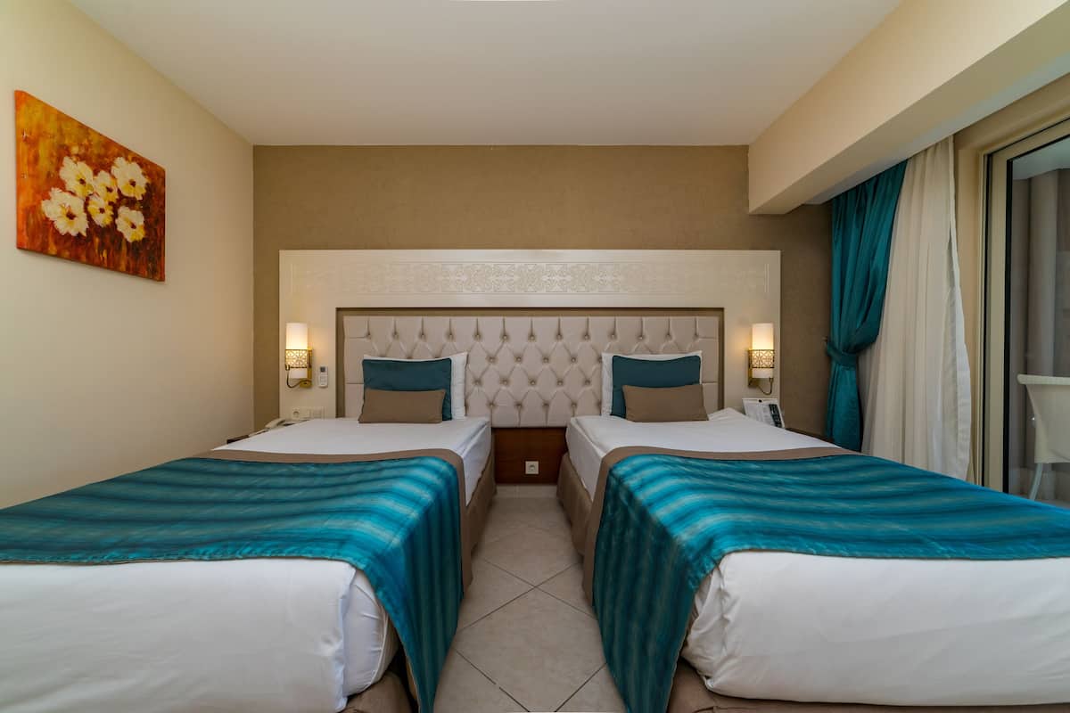 Habitación de hotel con dos camas, un cabecero capitonado, lámparas de noche y un cuadro en la pared.