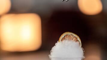 A glass with a red beverage and a slice of orange on top, placed on a wooden surface with a lit candle in the background.