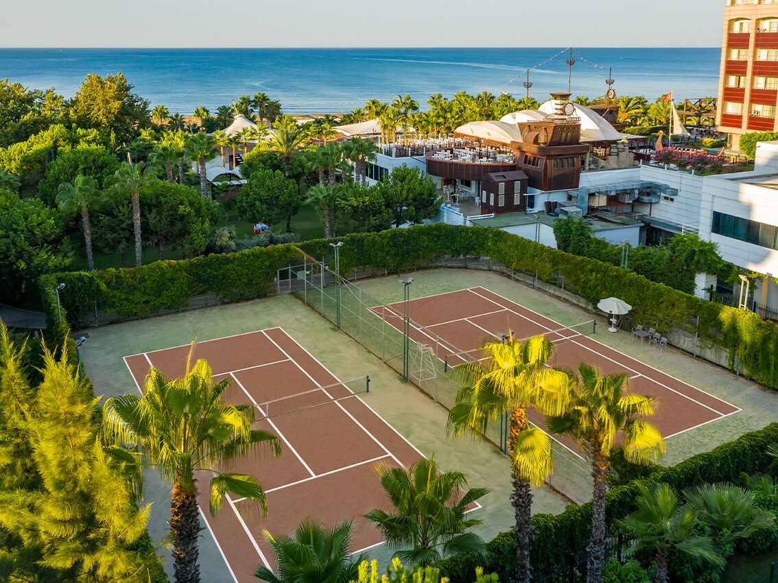 A tennis court surrounded by lush greenery and a view of the ocean.