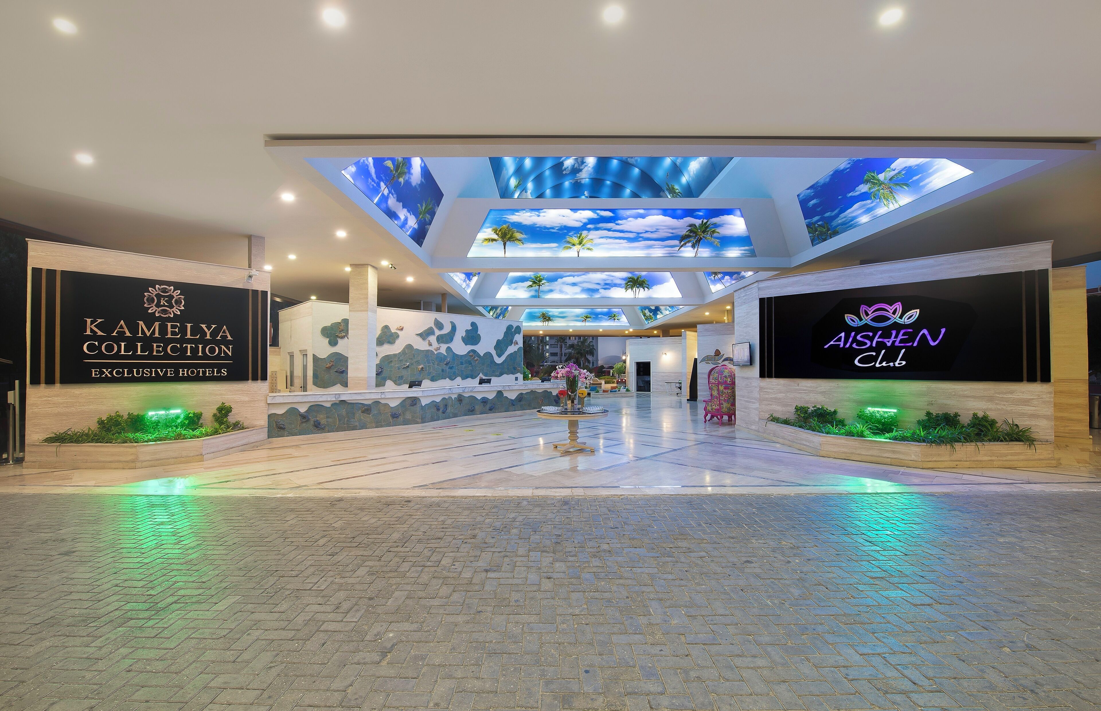A hotel lobby with a modern design, featuring a central atrium with a ceiling display of a tropical sky and palm trees.