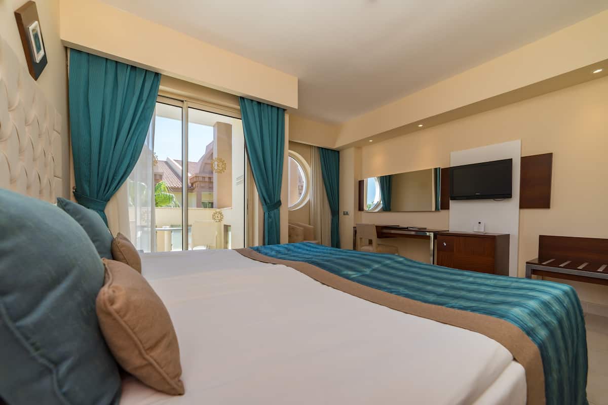 Habitación de hotel con una cama grande, un escritorio, un televisor y vistas al exterior.