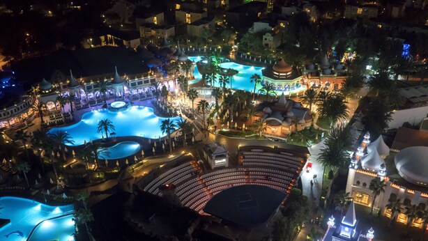 An aerial view of a resort with multiple swimming pools, a large amphitheater, and various resort buildings. - Kamelya Aishen Club (Manavgat)