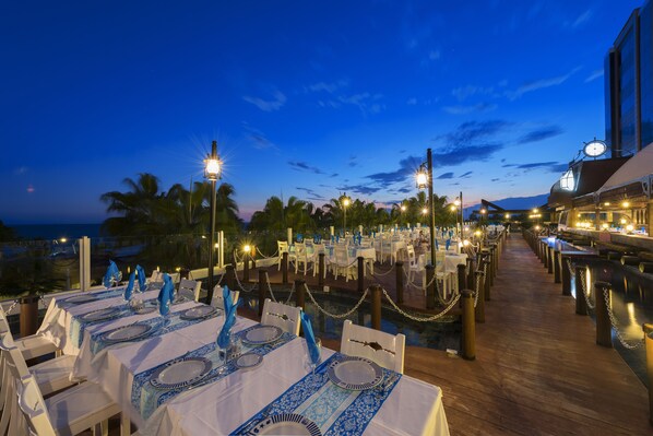 An outdoor dining area with tables set for guests, featuring a view of the ocean and palm trees. - Kamelya Aishen Club (Manavgat)