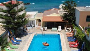 A rectangular pool with a small boat, surrounded by lounge chairs and a view of the ocean. - Haris Apartments (Hersonissos)