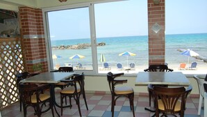 A beachside restaurant with outdoor seating, a view of the sea, and a tiled floor. - Haris Apartments (Hersonissos)